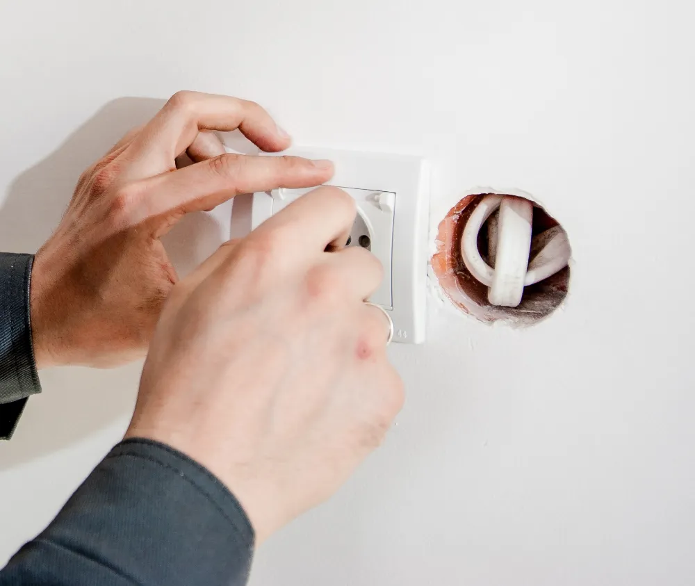 Elektrikari baten eskuak entxufe bat jartzen horma zuri batean